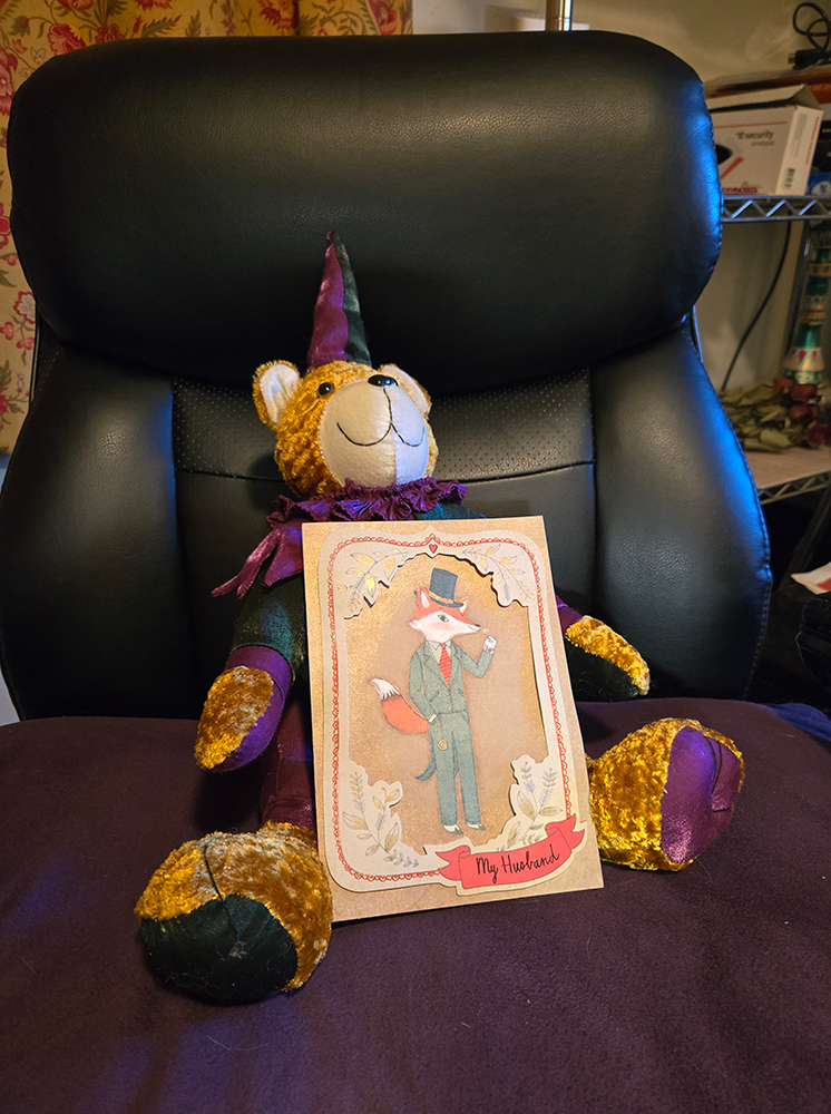 Stuffed Christmas bear with greet card, positioned on an office chair.